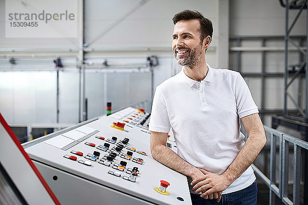 Lächelnder Mann an einer Schalttafel in einer Fabrik