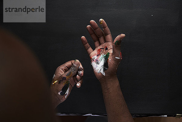 Schmutzige Hände des Künstlers mit bunten Farben vor schwarzem Hintergrund