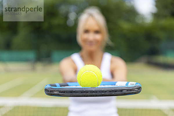 Nahaufnahme einer Frau  die im Tennisclub einen Tennisschläger mit einem Ball in der Hand hält