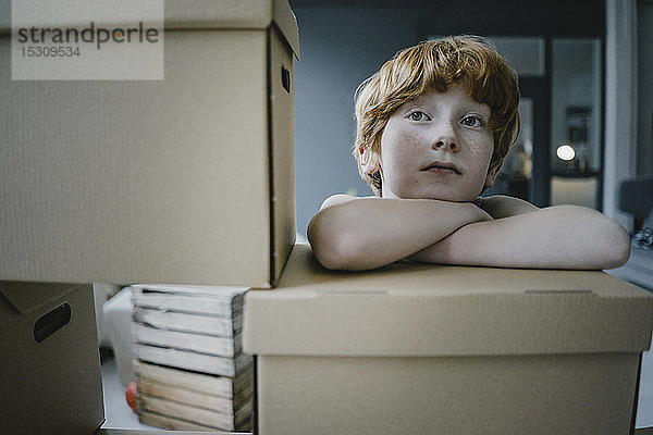 Porträt eines rothaarigen Jungen  der sich an einen Pappkarton lehnt