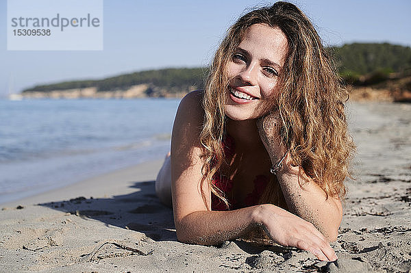 Porträt einer glücklichen jungen Frau am Strand liegend