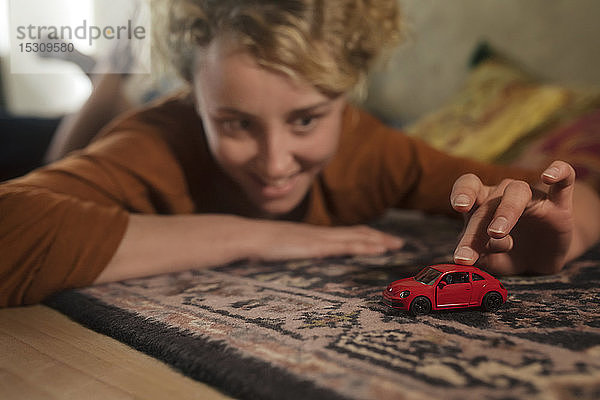 Junge Frau liegt auf Teppich und spielt mit rotem Spielzeugauto