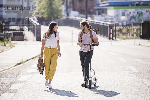 Junges Paar mit Elektroroller läuft und spricht auf der Straße