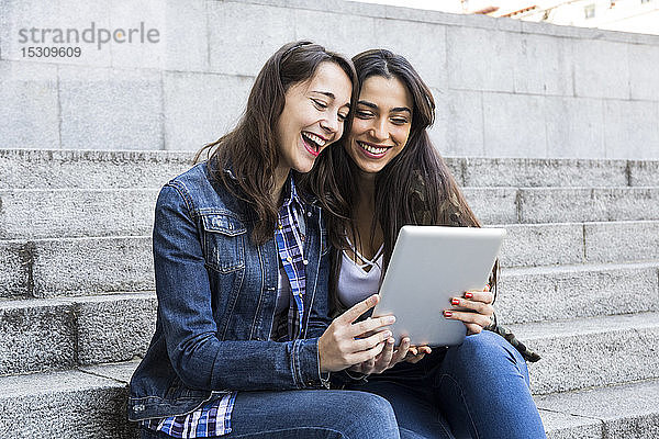 Glückliche junge Frauen schauen Tablet an  die in Madrid  Spanien  gemeinsam auf Stufen sitzen