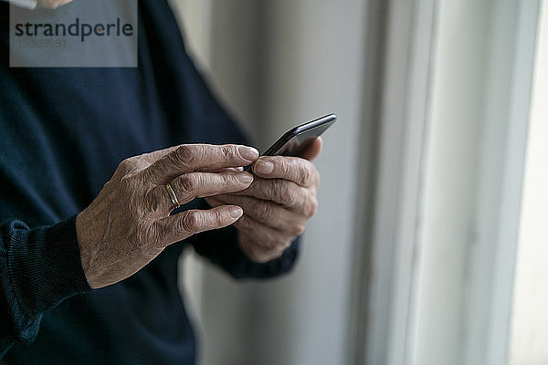 Nahaufnahme eines älteren Mannes bei der Benutzung eines Mobiltelefons zu Hause