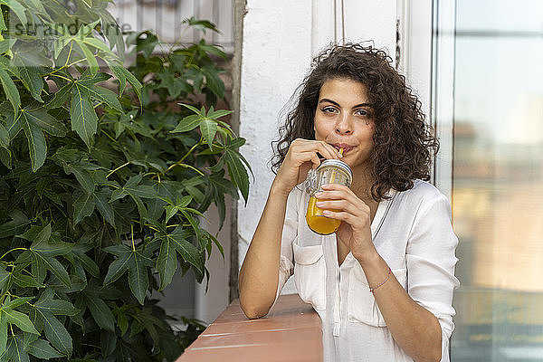 Porträt einer jungen Frau  die ein Glas Orangensaft trinkt