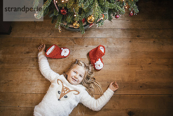 Lächelndes Mädchen unter dem Weihnachtsbaum liegend