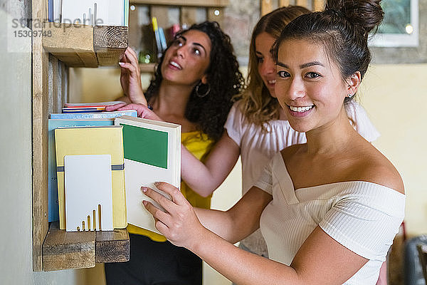 Drei lächelnde junge Frauen an einem Bücherregal