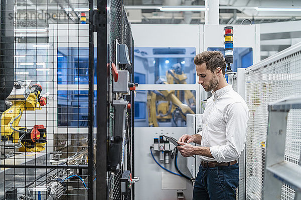 Geschäftsmann mit Tablette an einem Roboter in einer modernen Fabrik