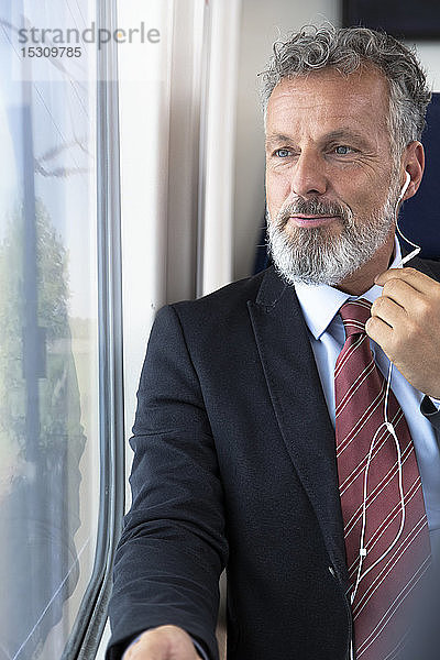 Älterer Geschäftsmann im Zug sitzend  mit Kopfhörern