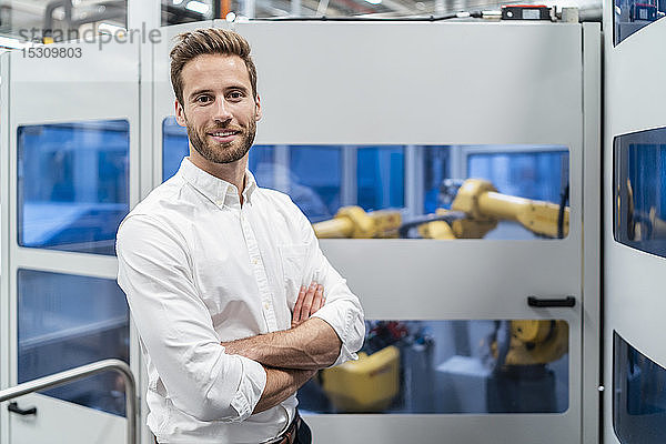 Porträt eines lächelnden Geschäftsmannes vor einem Roboter in einer modernen Fabrik