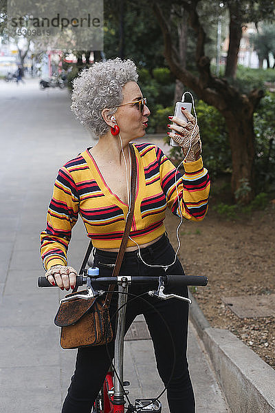 Modische reife Frau mit Fahrrad und Smartphone