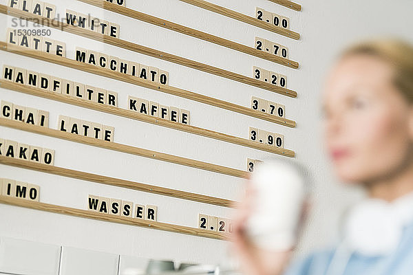 Preistafel in einem Kaffeehaus mit Kunden  die eine Tasse Kaffee tragen