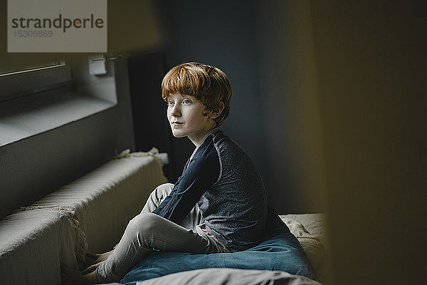 Porträt eines rothaarigen Jungen  der auf einer Couch sitzt und in die Ferne schaut