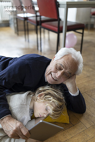 Großvater und Enkel liegen zu Hause mit einer Tablette auf dem Boden