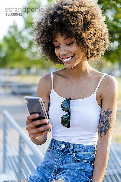 Porträt einer tätowierten jungen Frau im Sommer beim Blick auf ein Smartphone