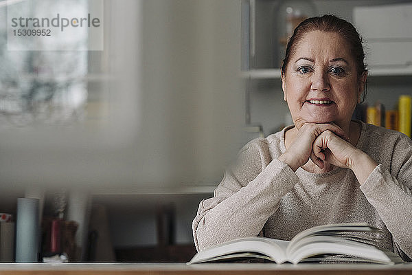 Porträt einer lächelnden älteren Frau mit Buch zu Hause