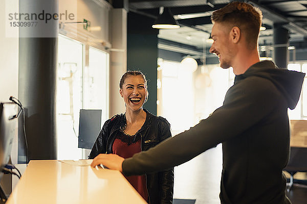 Lachende junge Frau im Gespräch mit dem Trainer an der Rezeption einer Sporthalle