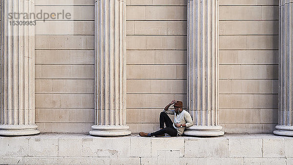 Mittelgroßer erwachsener Mann zwischen den Säulen sitzend