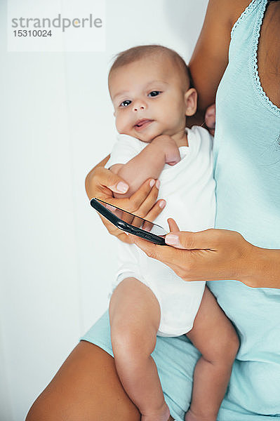 Mutter benutzt Smartphone und hält ihr Baby