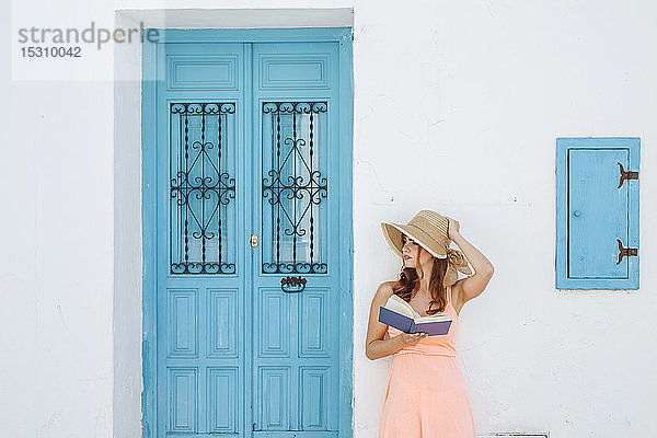 Rothaarige junge Frau mit Buch  die vor einem Haus steht und in die Ferne schaut  Frigiliana  Malaga  Spanien