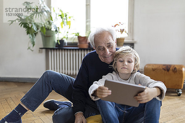 Grossvater und Enkel sitzen zu Hause auf dem Boden und benutzen ein Tablett