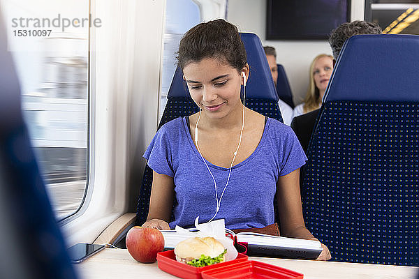 Teenagerin  die allein mit dem Zug reist  Musik hört  einen Imbiss isst