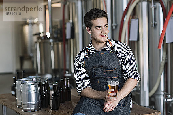 Junger Mann trinkt ein Bier in einer Brauerei