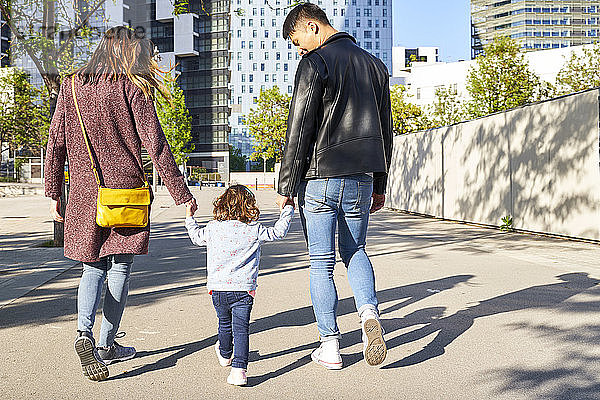 Eltern und kleines Mädchen halten sich an den Händen und gehen zusammen in Barcelona  Spanien