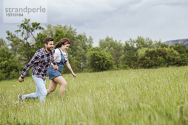 Junges Paar rennt Händchen haltend über ein Feld
