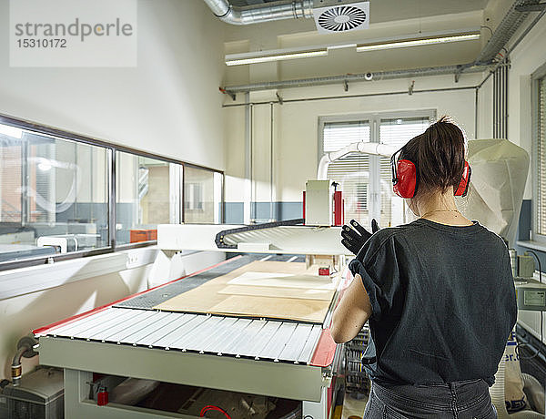 Rückansicht einer Frau an einer CNC-Maschine in der Werkstatt