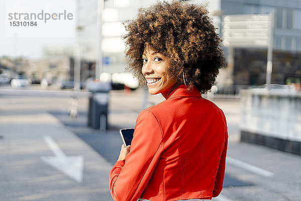 Porträt einer lächelnden jungen Frau mit Smartphone in modischer roter Anzugsjacke