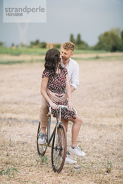 Küssendes Paar mit handgefertigtem Rennrad auf Stoppelfeld