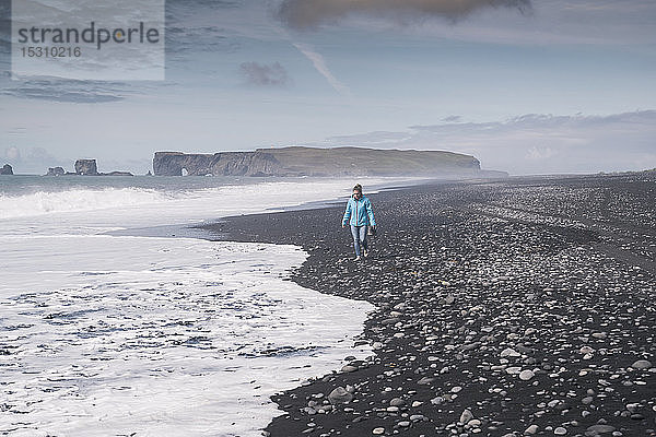 Junge Frau geht barfuss an einem Lavastrand in Island