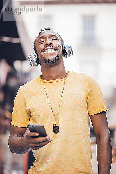 Porträt eines glücklichen Mannes  der mit Kopfhörer und Smartphone Musik hört