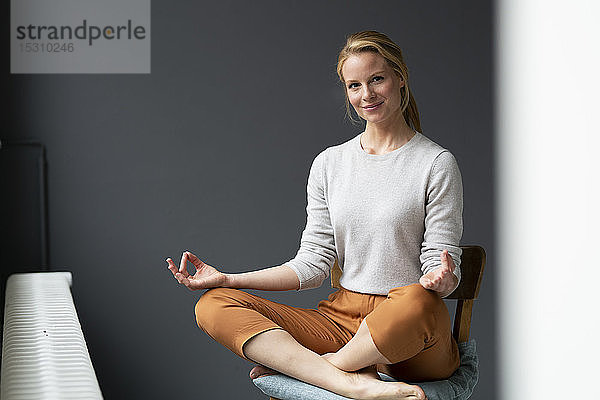Junge Frau  die im Büro auf einem Stuhl sitzt und Yoga praktiziert