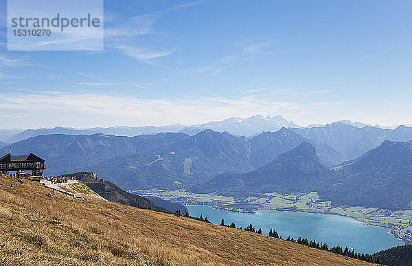 Schafbergbahn auf Berggipfel mit Blick auf Wolfgangsee und Dachsteingebirge vor blauem Himmel