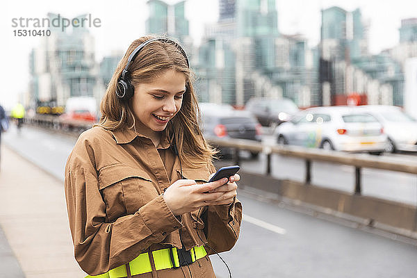 Glückliche junge Frau mit Kopfhörern und Handy in der Stadt  London  UK