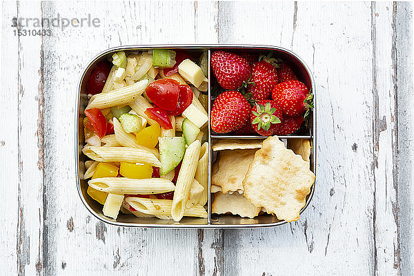 Nudelsalat  Erdbeeren und Cracker in Lunchbox auf Holztisch