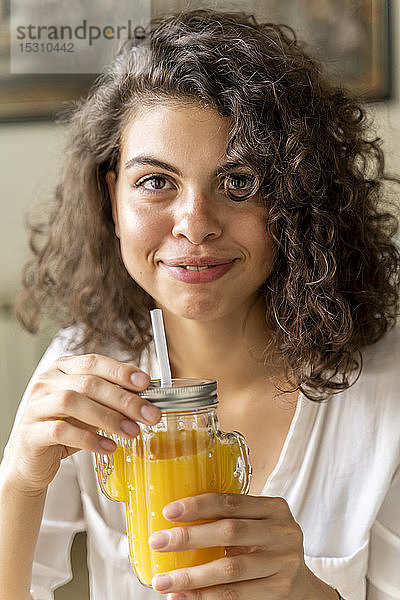 Porträt einer lächelnden jungen Frau mit einem Glas Orangensaft