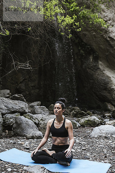 Frau praktiziert Yoga und meditiert am Wasserfall