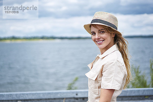 Porträt einer lächelnden Frau mit Hut am Seeufer