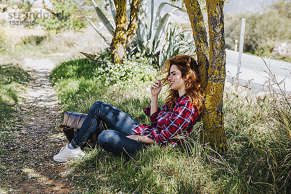 Rothaarige Frau mit Zigarettenpause unter einem Baum