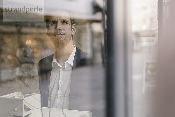 Porträt eines Geschäftsmannes mit Architekturmodell  der aus dem Fenster schaut