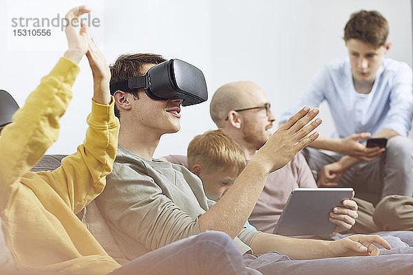 Glückliche Familie sitzt auf der Couch  benutzt VR-Brille und mobile Geräte