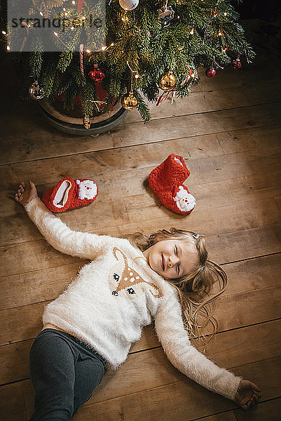 Lächelndes Mädchen mit geschlossenen Augen unter dem Weihnachtsbaum liegend