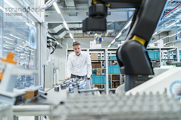 Geschäftsmann in einer modernen Fabrikhalle mit Blick auf Roboter