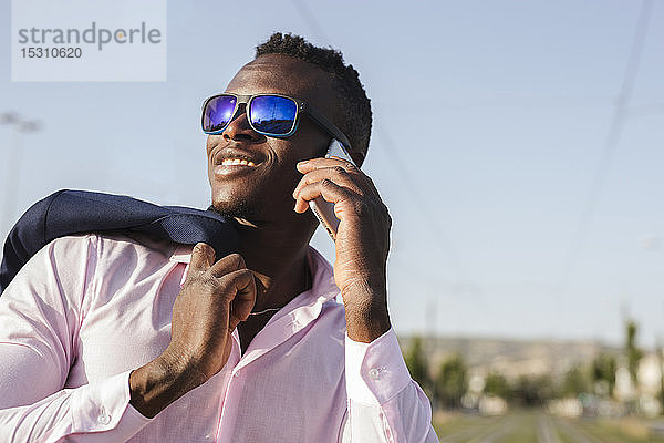 Junger Geschäftsmann mit Sonnenbrille benutzt draußen sein Smartphone