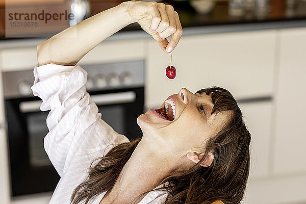 Glückliche Frau isst zu Hause in der Küche eine Kirsche