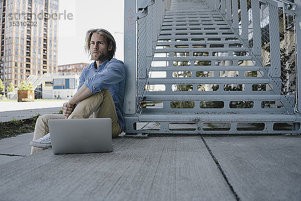 Junger Mann sitzt mit Laptop an der Treppe